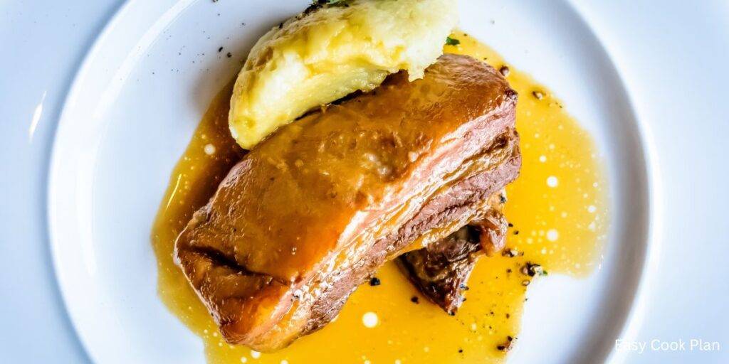 braised pork belly with potato on a white plate, with braised sauce.