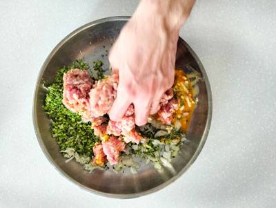 mixing ground pork and broccoli in a stainless steel bowl