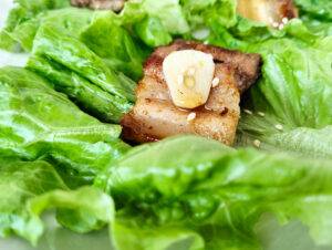 a piece of pork belly and a slice of raw garlic lying on a lettuce leaf