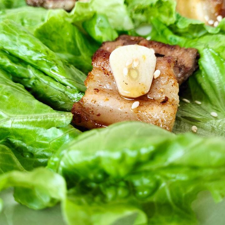 a piece of pork belly and a slice of raw garlic lying on a lettuce leaf